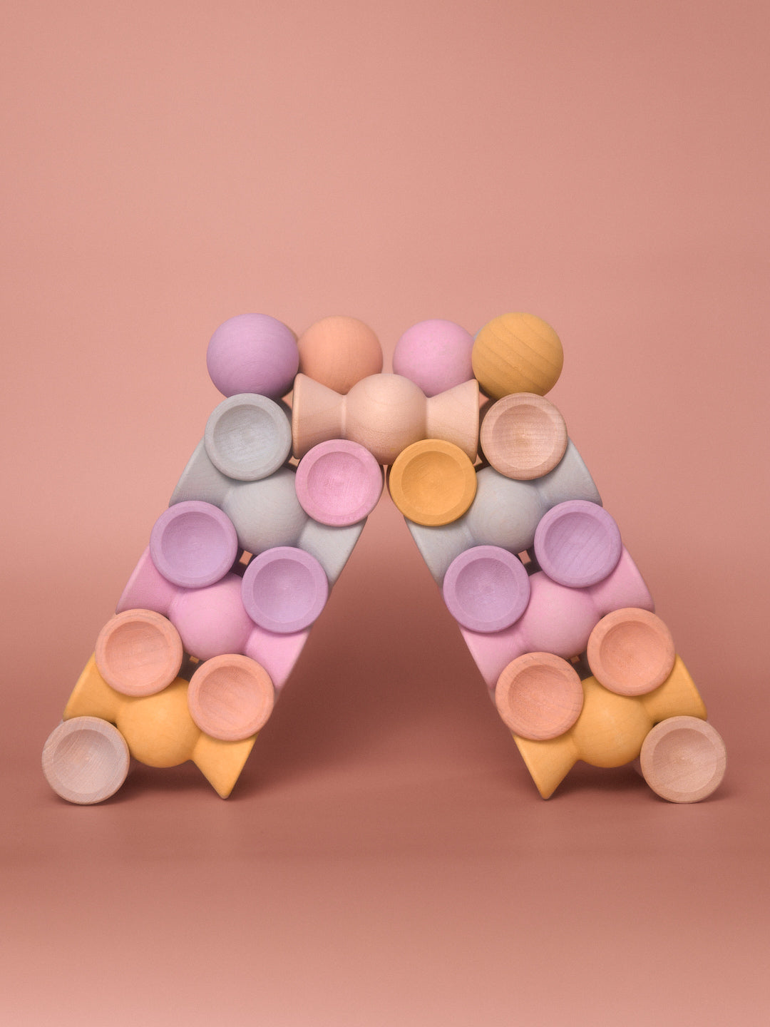 Chill Pepper Sweets Peachy Pastels wooden pieces balanced in a triangular arch on a pink background.
