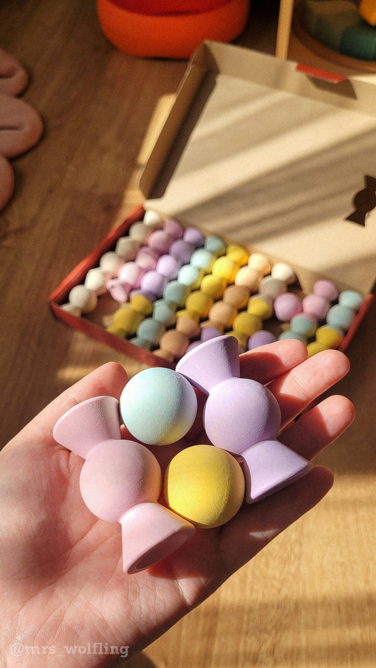 Hand holding Chill Pepper Sweets Peachy Pastels wooden sweets and gumballs, with more pieces arranged on a table behind.
