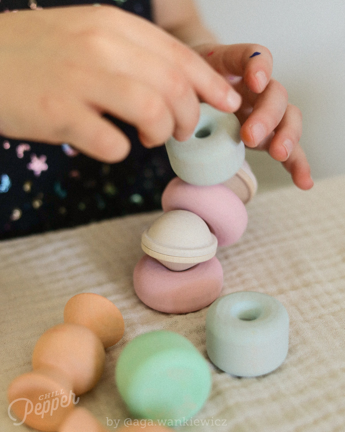 Child stacking Chill Pepper Treats pastel wooden pieces on a table, with doughnut and sweet shapes in the foreground.