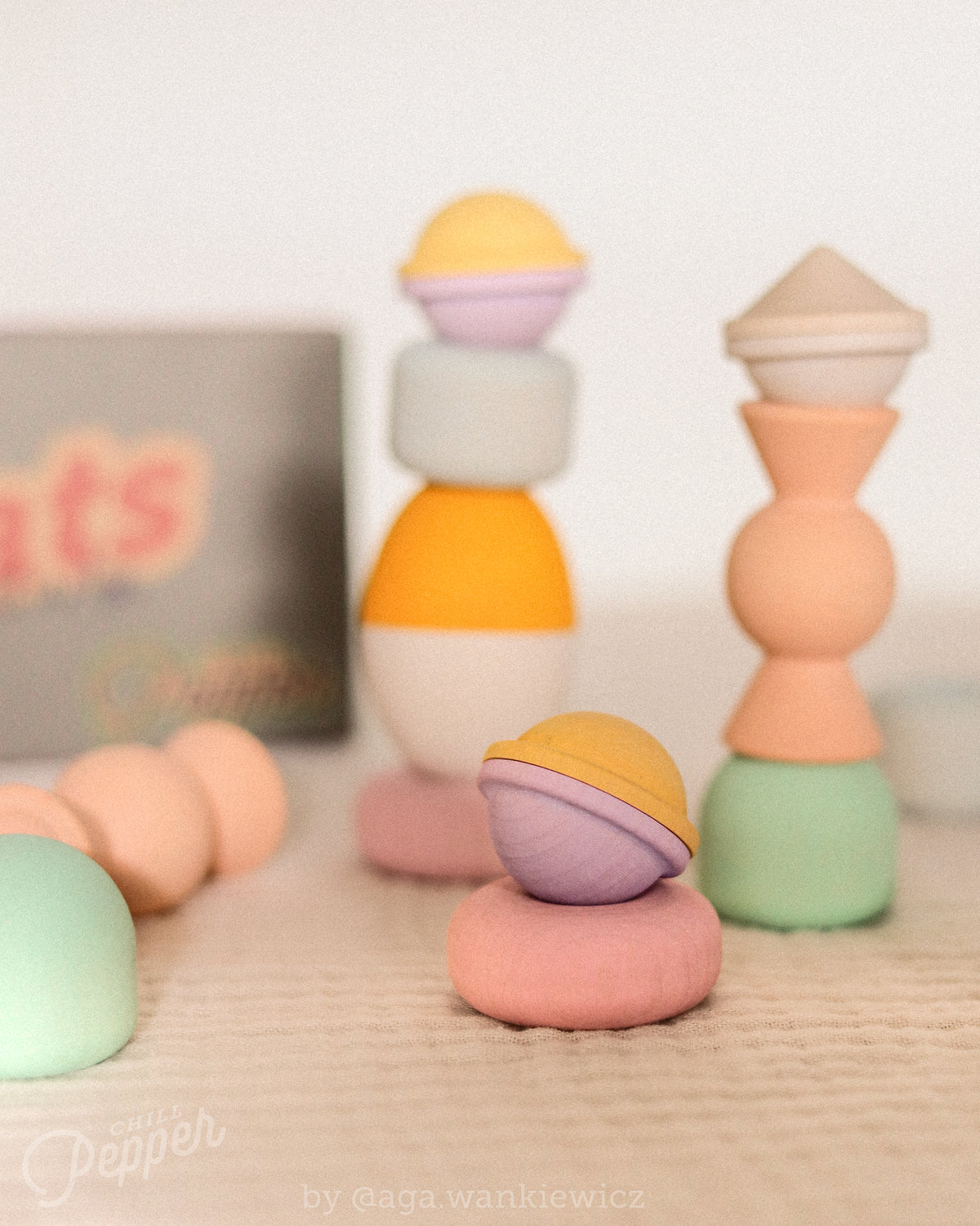 Chill Pepper Treats wooden toys arranged in three colourful stacks, with a yellow and lavender piece balanced on a pink ring in front.