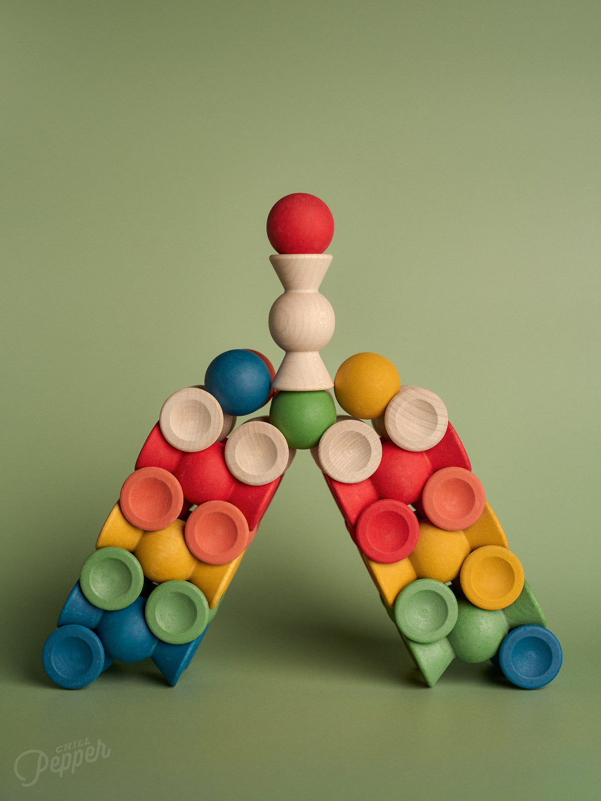 Chill Pepper Sweets Forest Fruits wooden pieces balanced in a triangular arch on a green background.